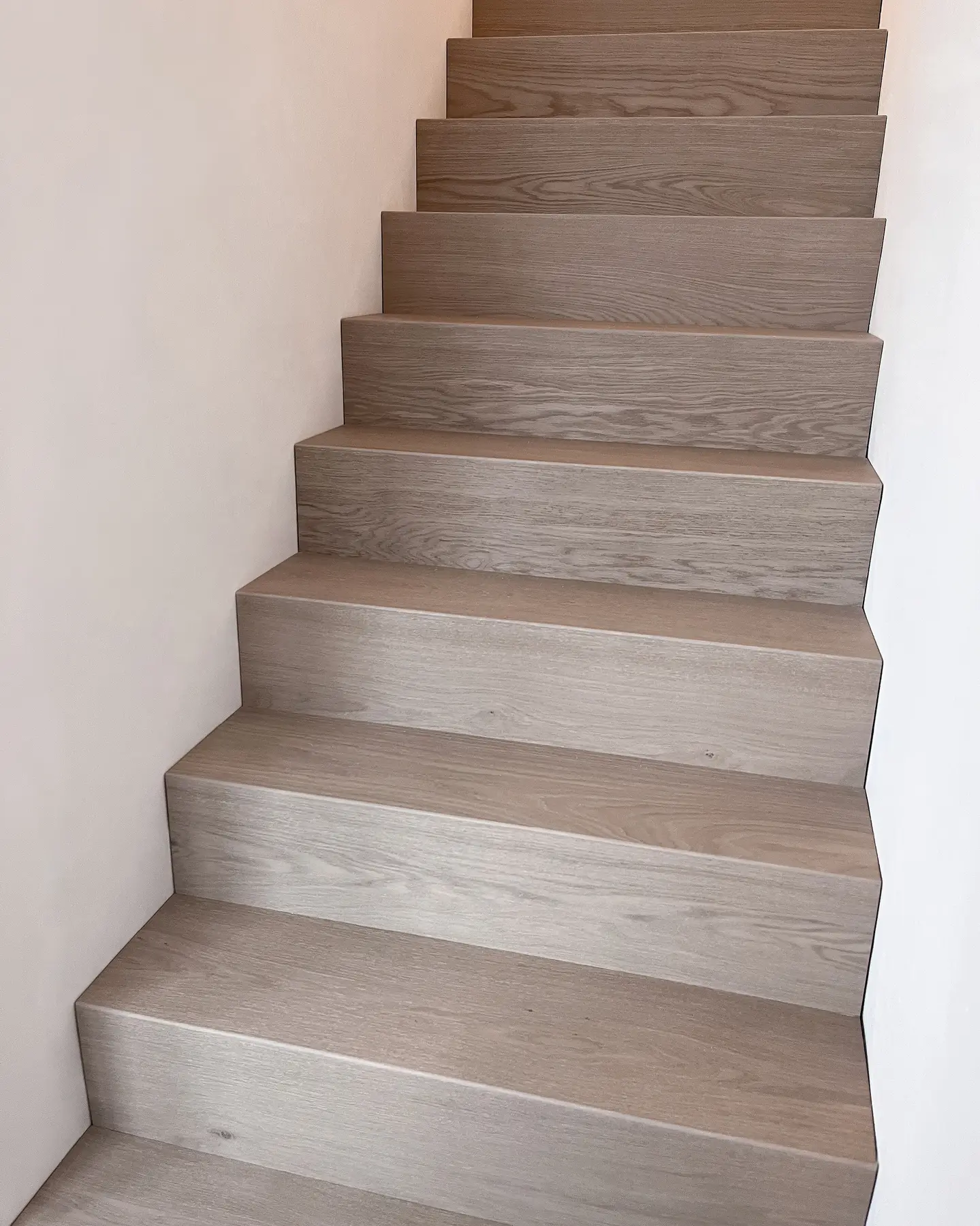 Rechte eiken trap langs een witte wand
